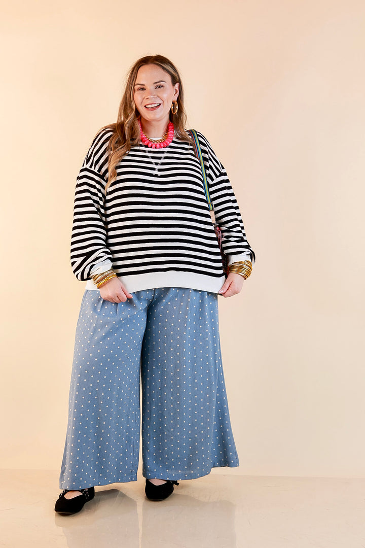 Model wearing a black and ivory striped drop shoulder pullover with a beaded necklace and black flats.