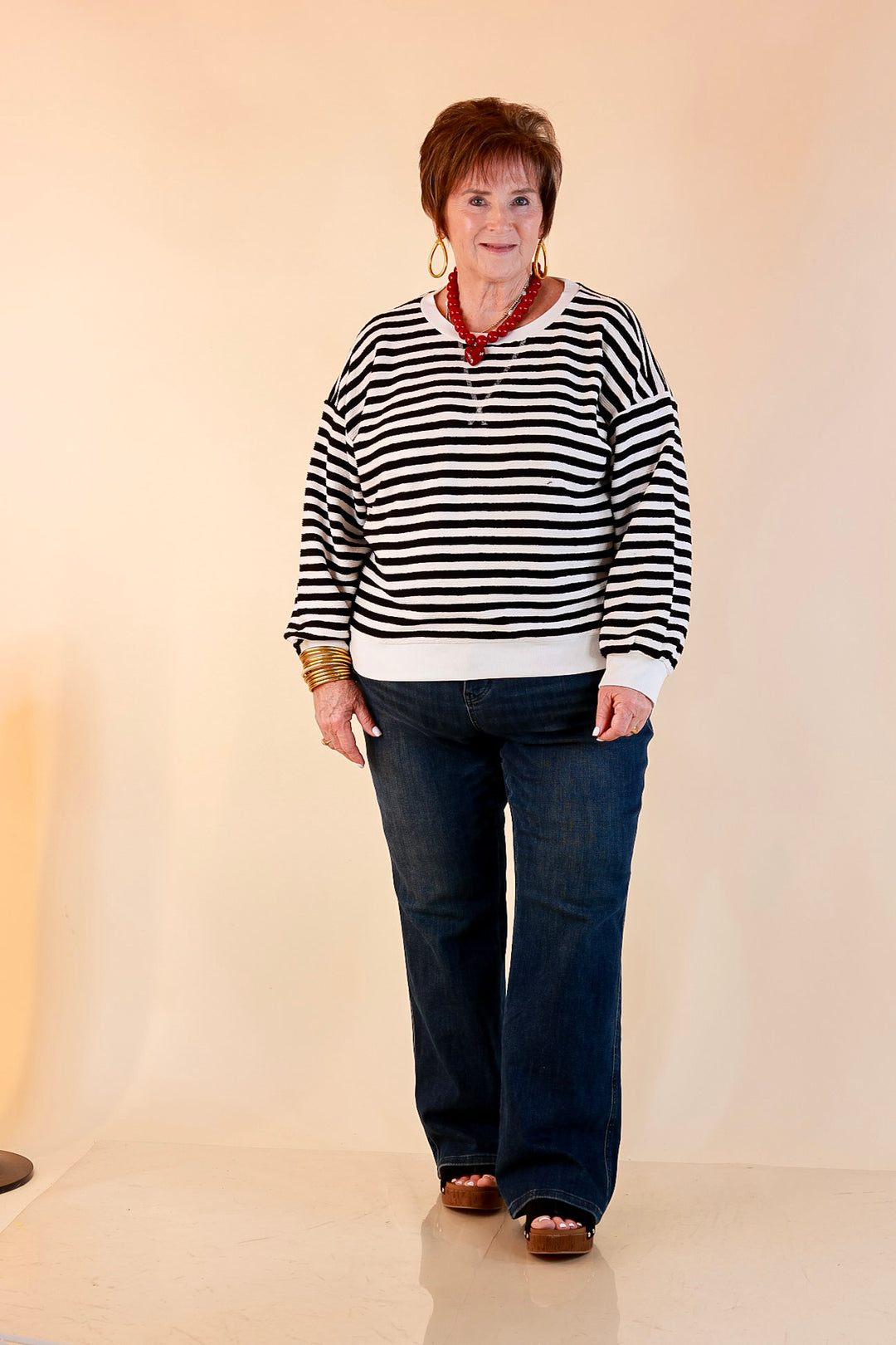 Model wearing a black and ivory striped pullover with a beaded necklace, dark wash flare jeans and platform sandals.