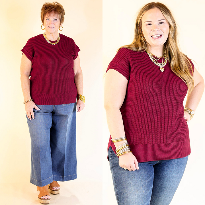 Two women wearing maroon sweater tops and blue jeans against a plain background