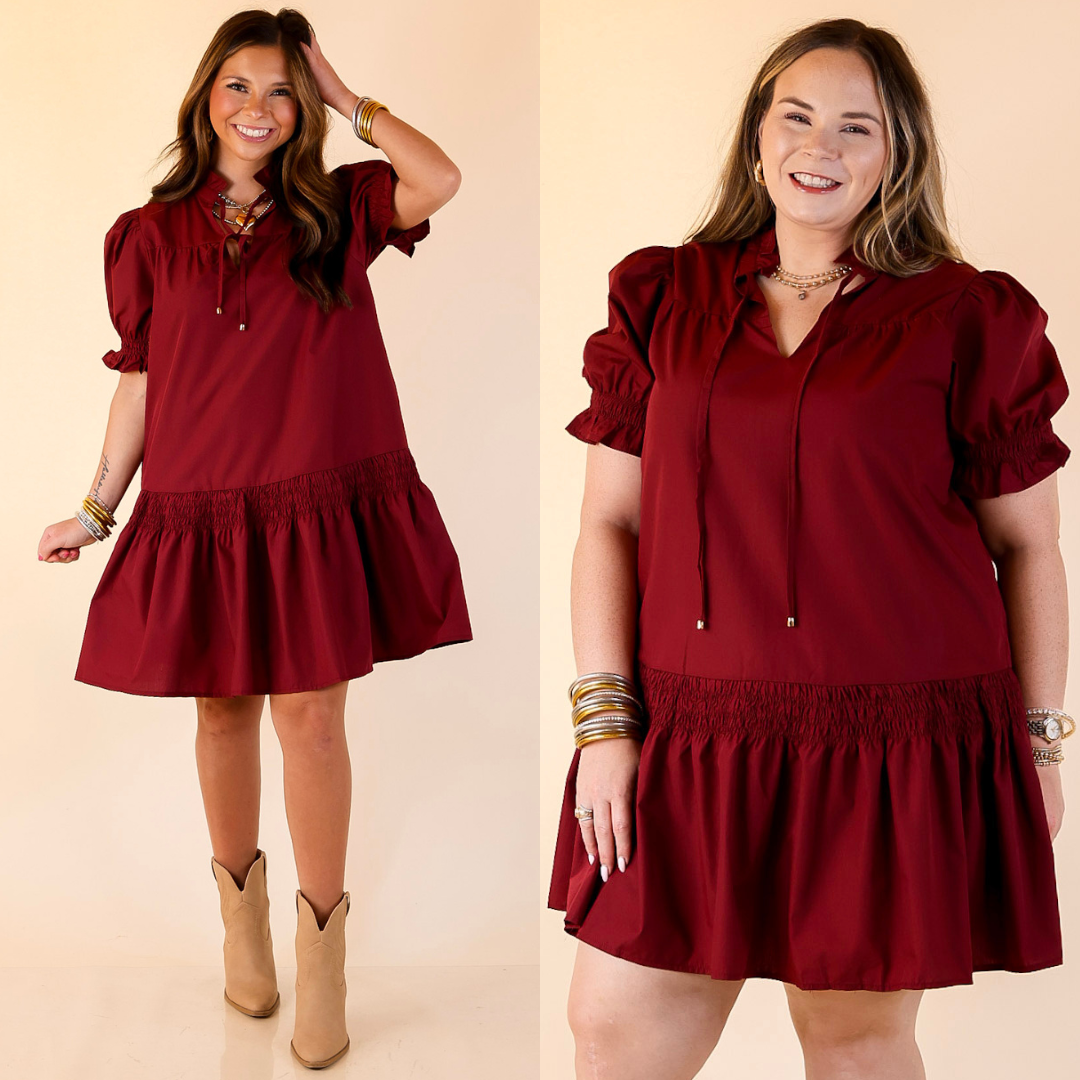 Woman wearing a maroon dress with puffed sleeves on a beige background