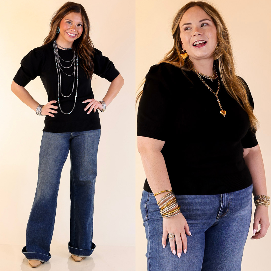 Two women wearing black tops and blue jeans with jewelry on a plain background