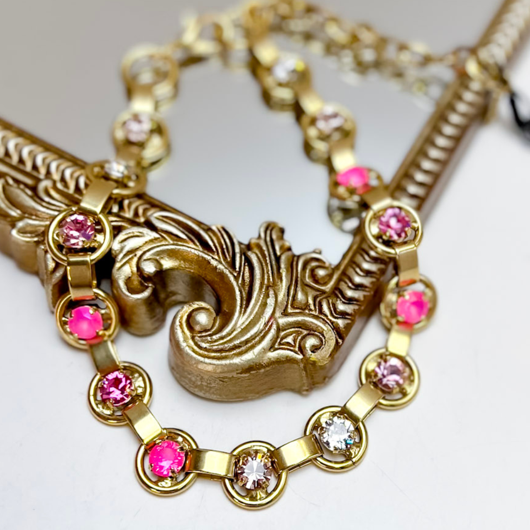 Gold and pink necklace on a gold mirror.