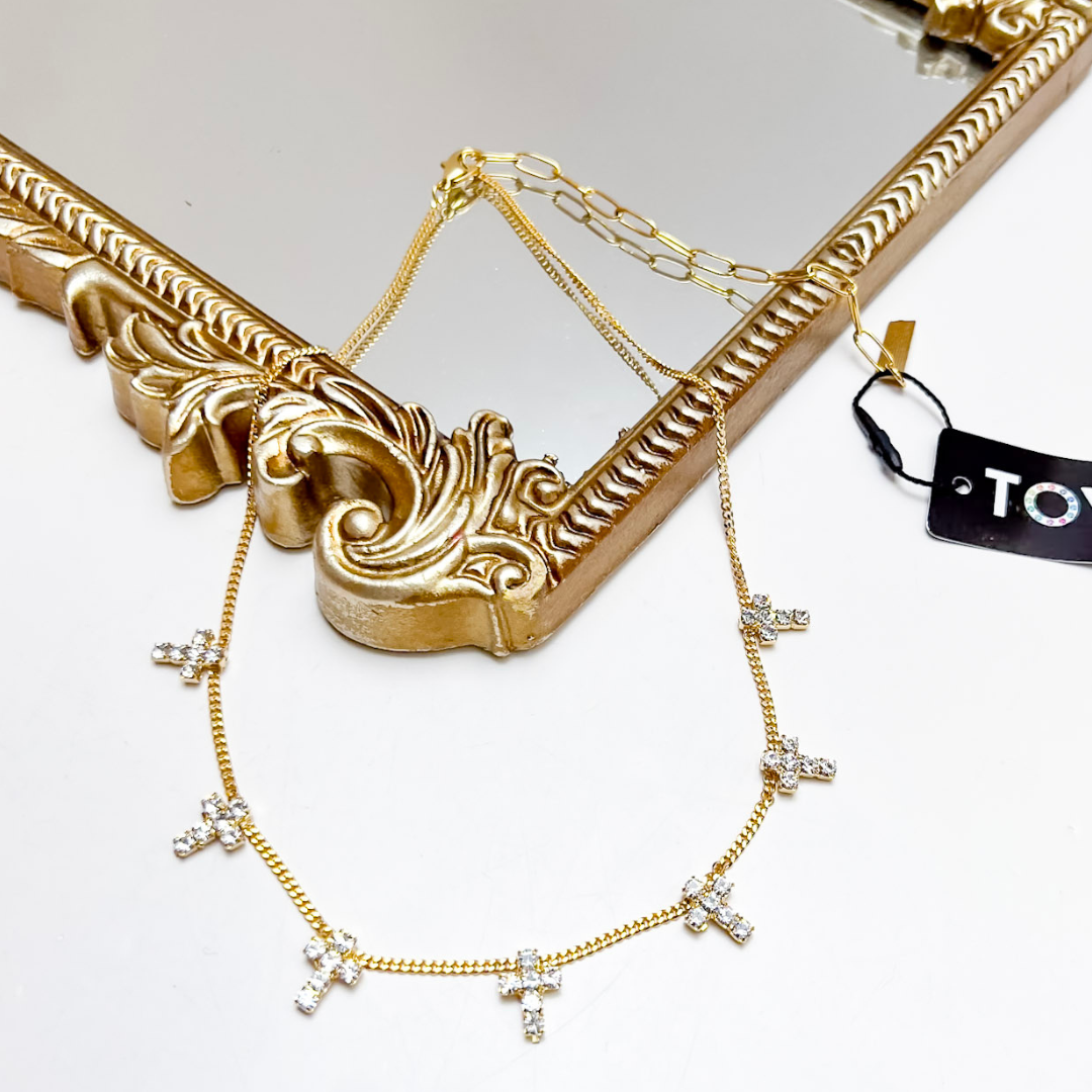Gold necklace with diamond-like pendants on a decorative gold stand with a visible brand tag.