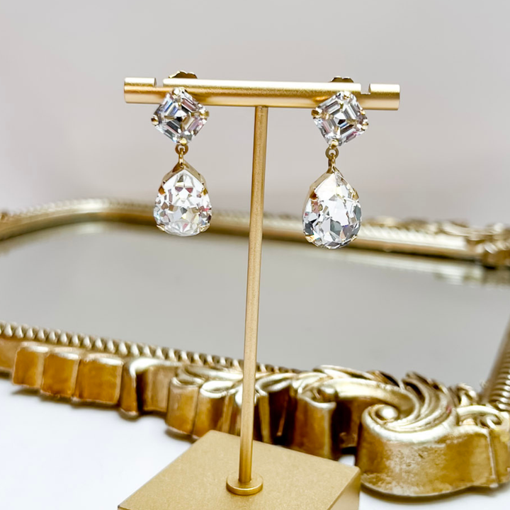 Gold earrings on a decorative stand with a mirror background