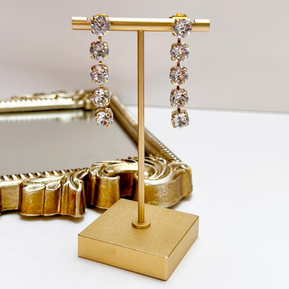 Gold earring stand with crystal earrings on a white surface