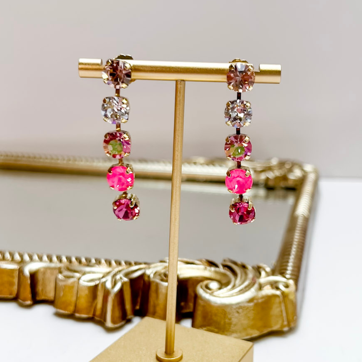 Earrings with pink and clear gemstones on a gold stand against a white background