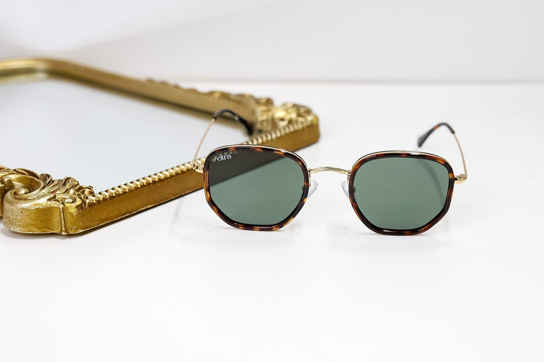 Gold-framed sunglasses with green lenses on a white surface