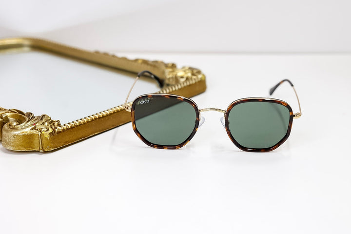Gold-framed sunglasses with green lenses on a white surface