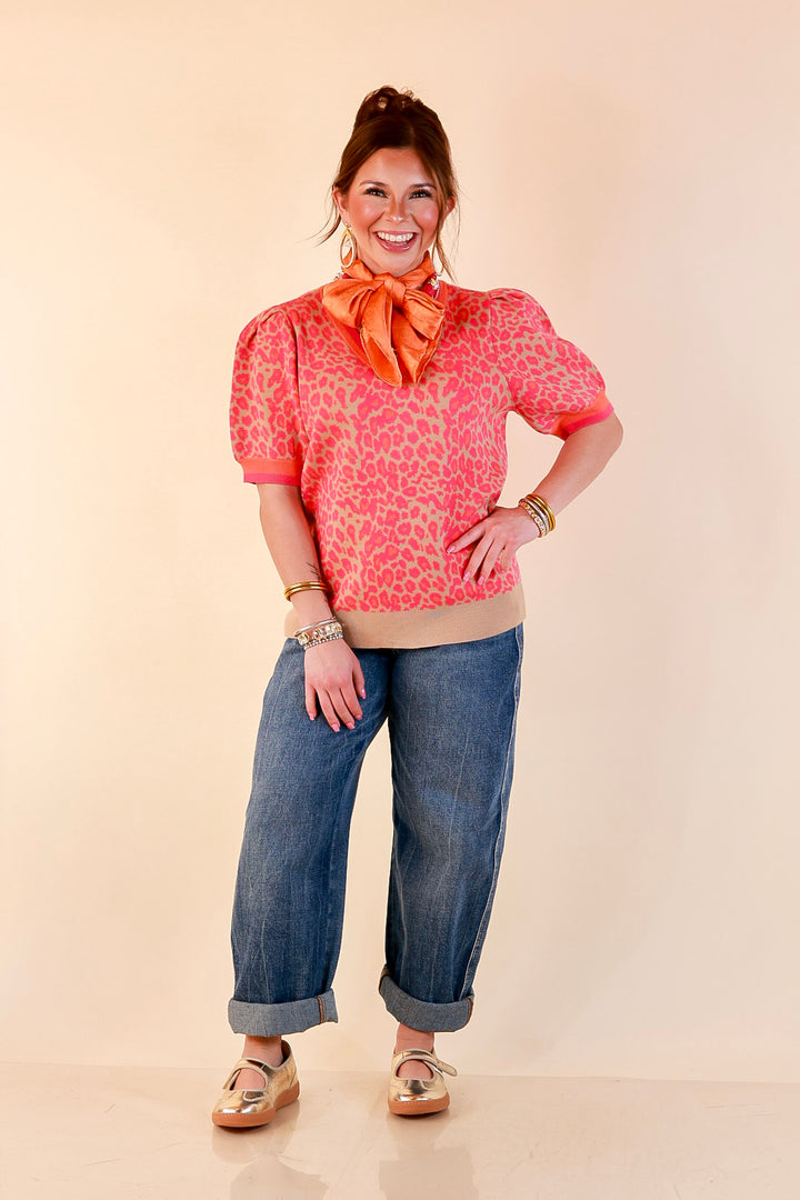 Model wearing a pink and orange leopard print puff sleeve sweater on a tan base with an orange silk scarf, cuffed wide-leg jeans and gold flats.