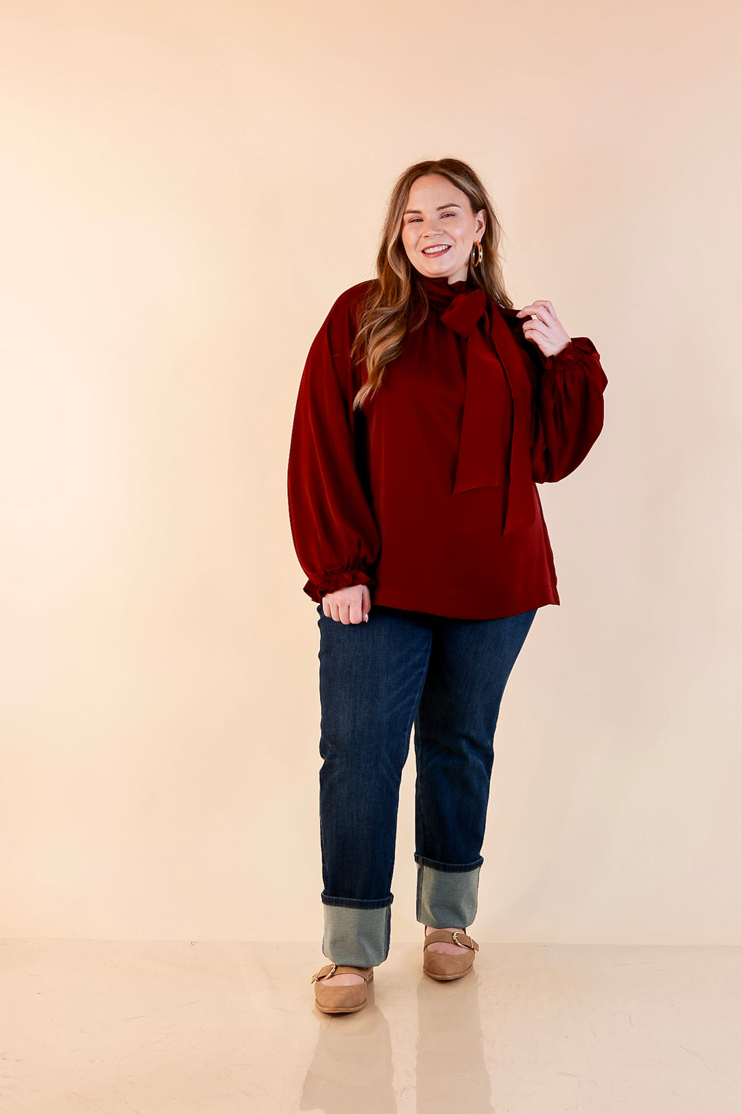 Model wearing a maroon long sleeve blouse with an oversized bow tie neckline, balloon sleeves and gathered cuffs.
