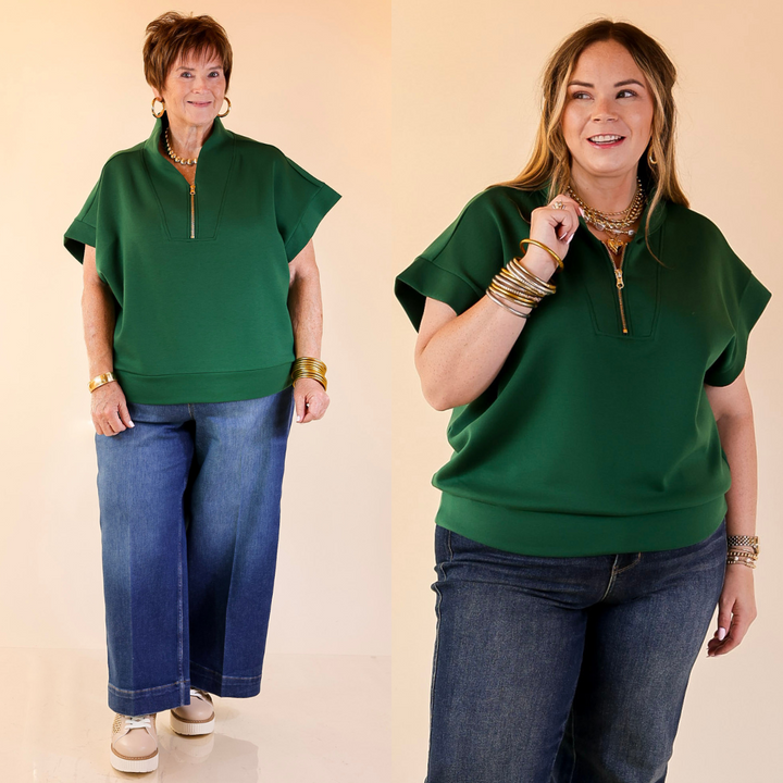 Two women wearing green scuba tops and blue jeans on a beige background