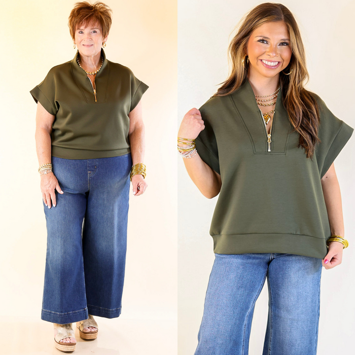 Two women wearing a olive green top and blue jeans against a plain background