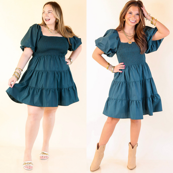 Two women wearing a teal dress with puff sleeves and ruffled layers on a plain background.