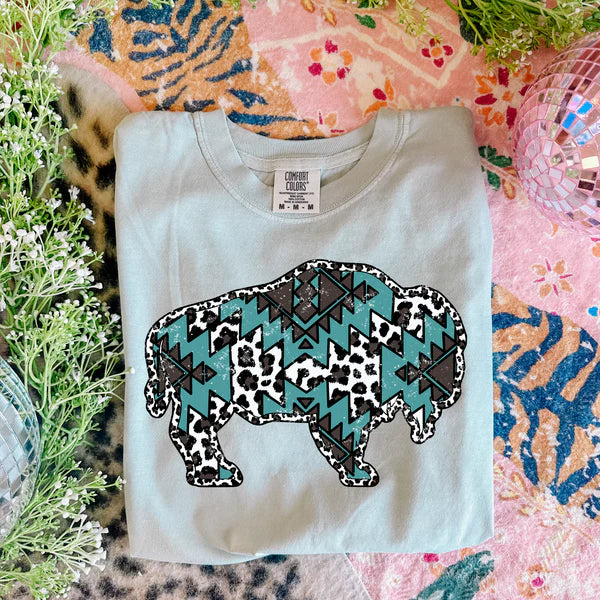 White t-shirt with a colorful bear design on a patterned surface with flowers.