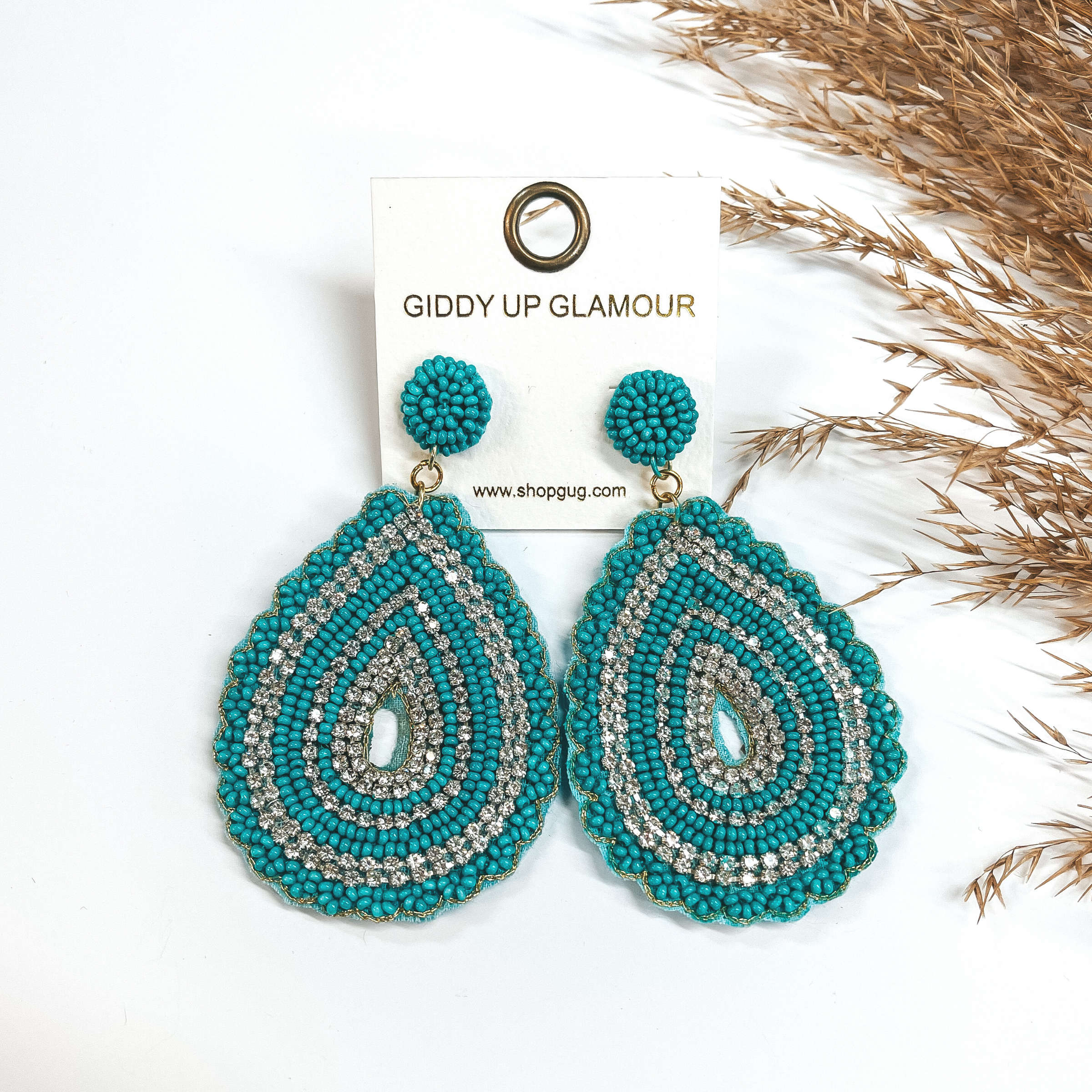 These earrings are wide teardrop earrings with bumps  all around with turquoise seed beads and clear  rhinestones. These earrings are taken on a white  background and a brown plant in the side as decor.