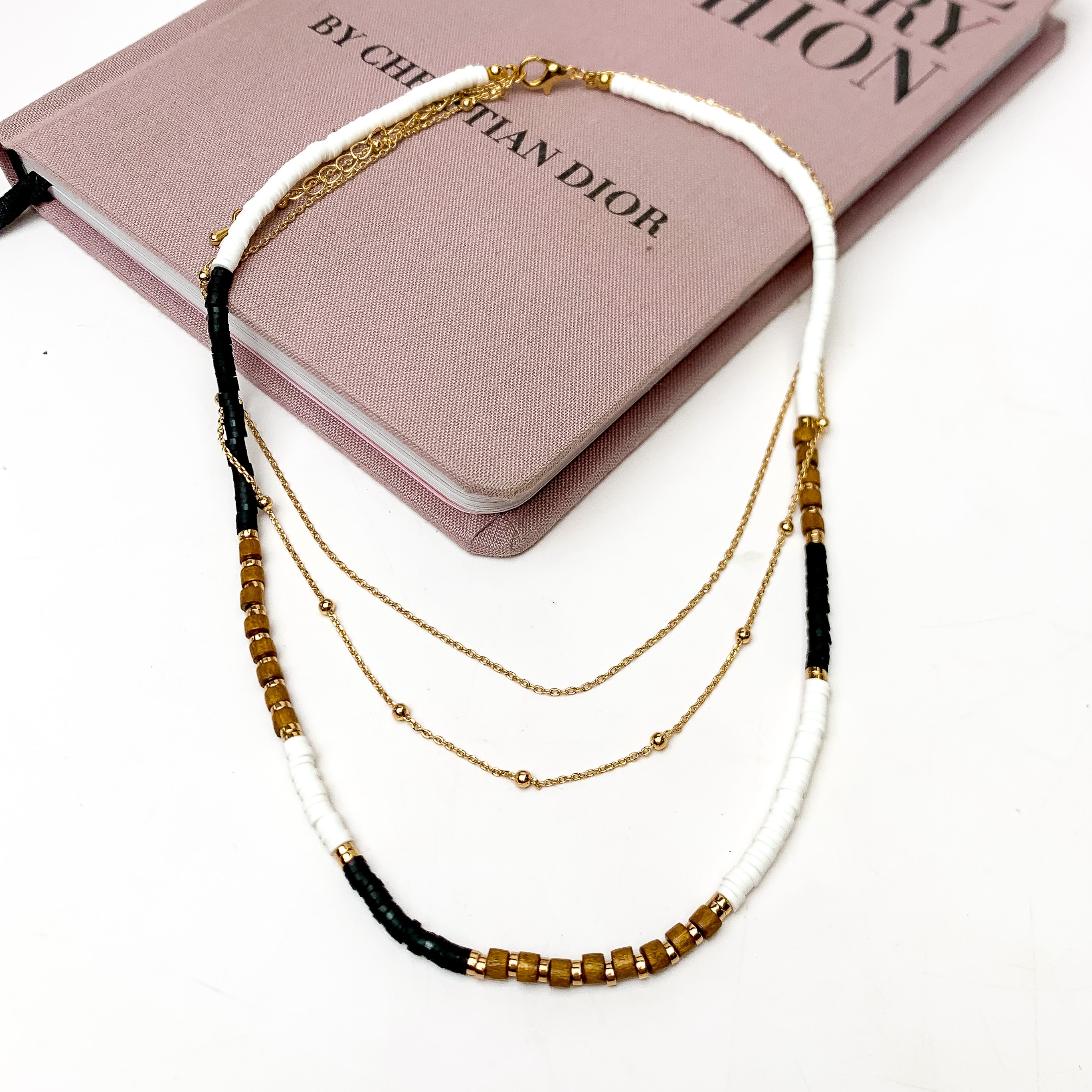Fall Coastal Multi Strand Gold Tone Necklace in Black. This necklace is pictured on a white background with part of it on a pink book.