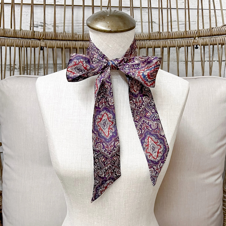 A patterned silk scarf with a purple, red, and blue paisley design, tied in a bow on a white fabric dress form mannequin.