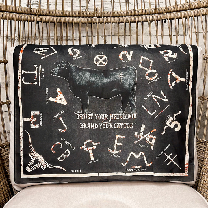 A scarf with a black background and white western-style graphics, including a cow silhouette, zodiac symbols, and the phrase &