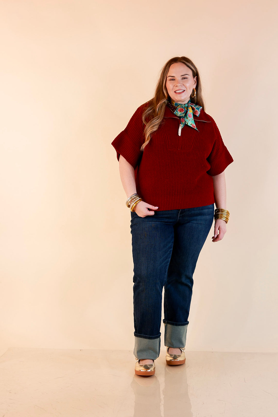 Model wearing a maroon ribbed half zip sweater with a floral scarf, cuffed dark wash jeans and gold flats.