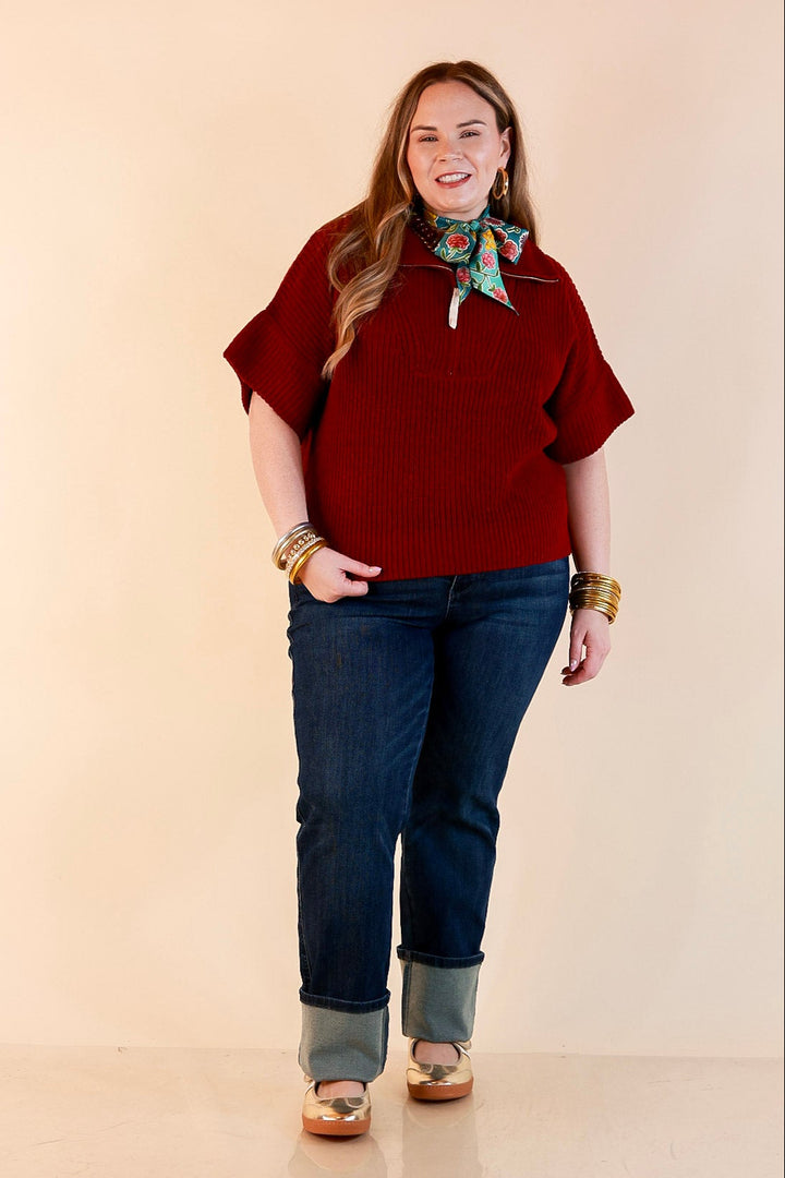 Model wearing a maroon ribbed half zip sweater with a floral scarf, cuffed dark wash jeans and gold flats.