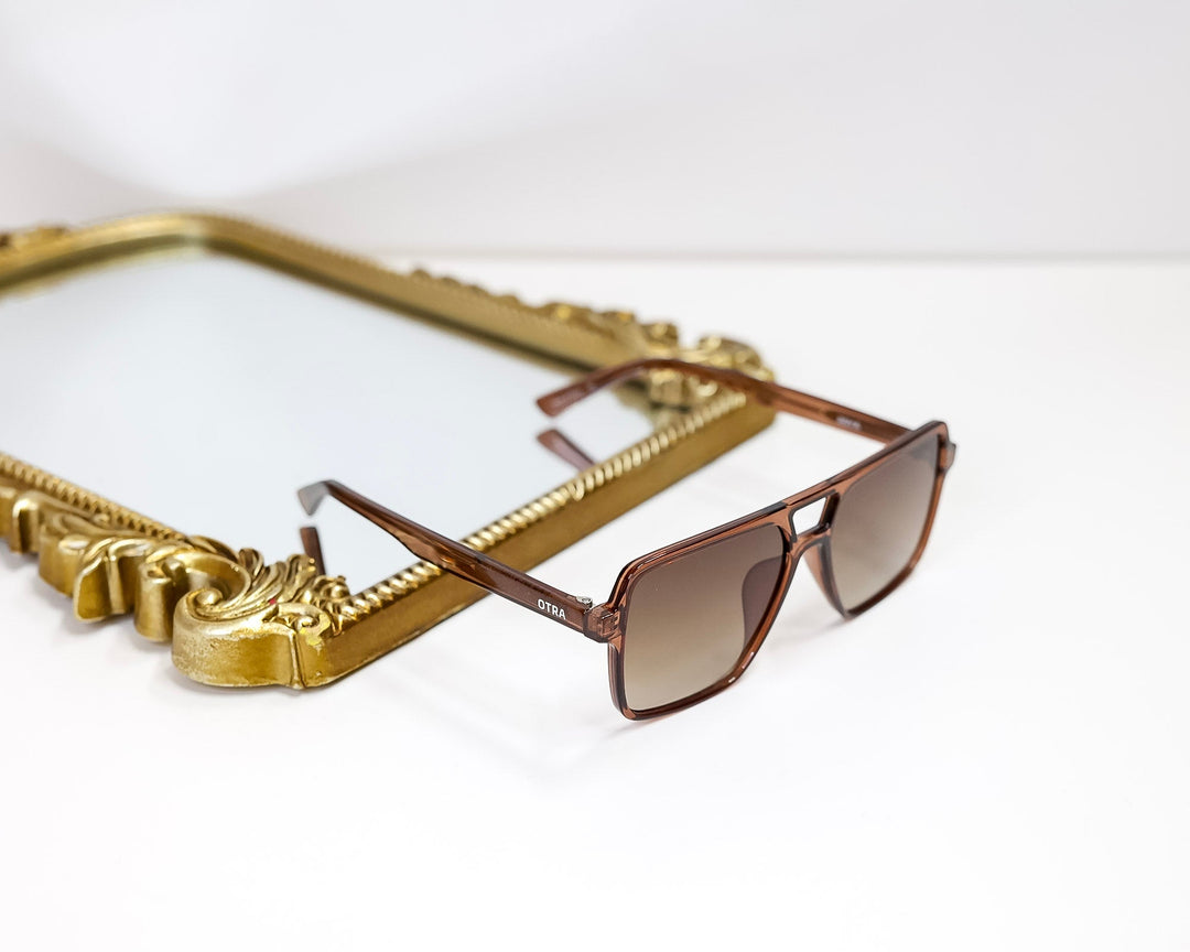 Brown sunglasses on a white surface with a gold chain and rectangular object in the background