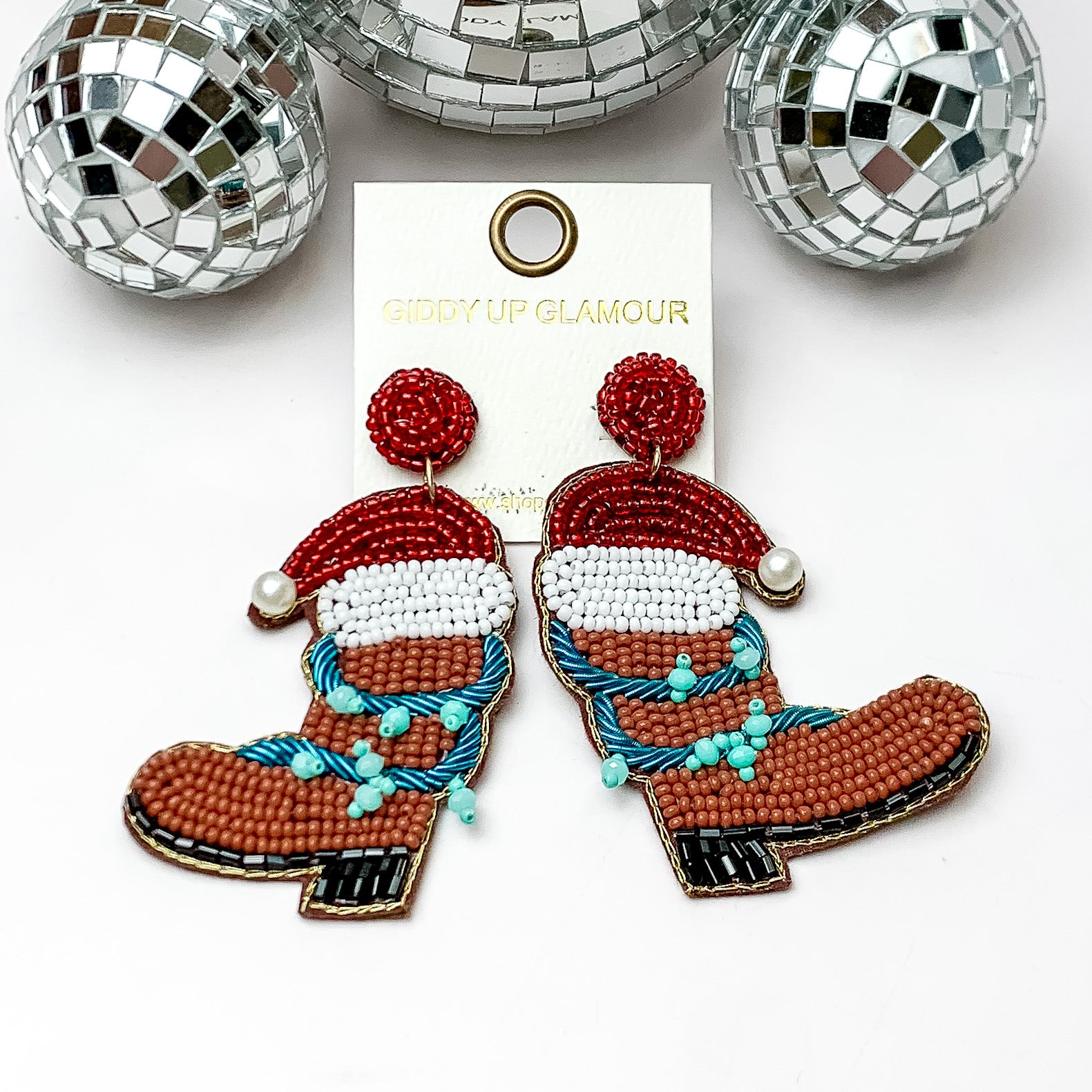 Brown beaded cowboy boot earrings with a red sant hat and turquoise blue lights wrapped around them. These earrings are pictured on a white background with disco balls at the top. 