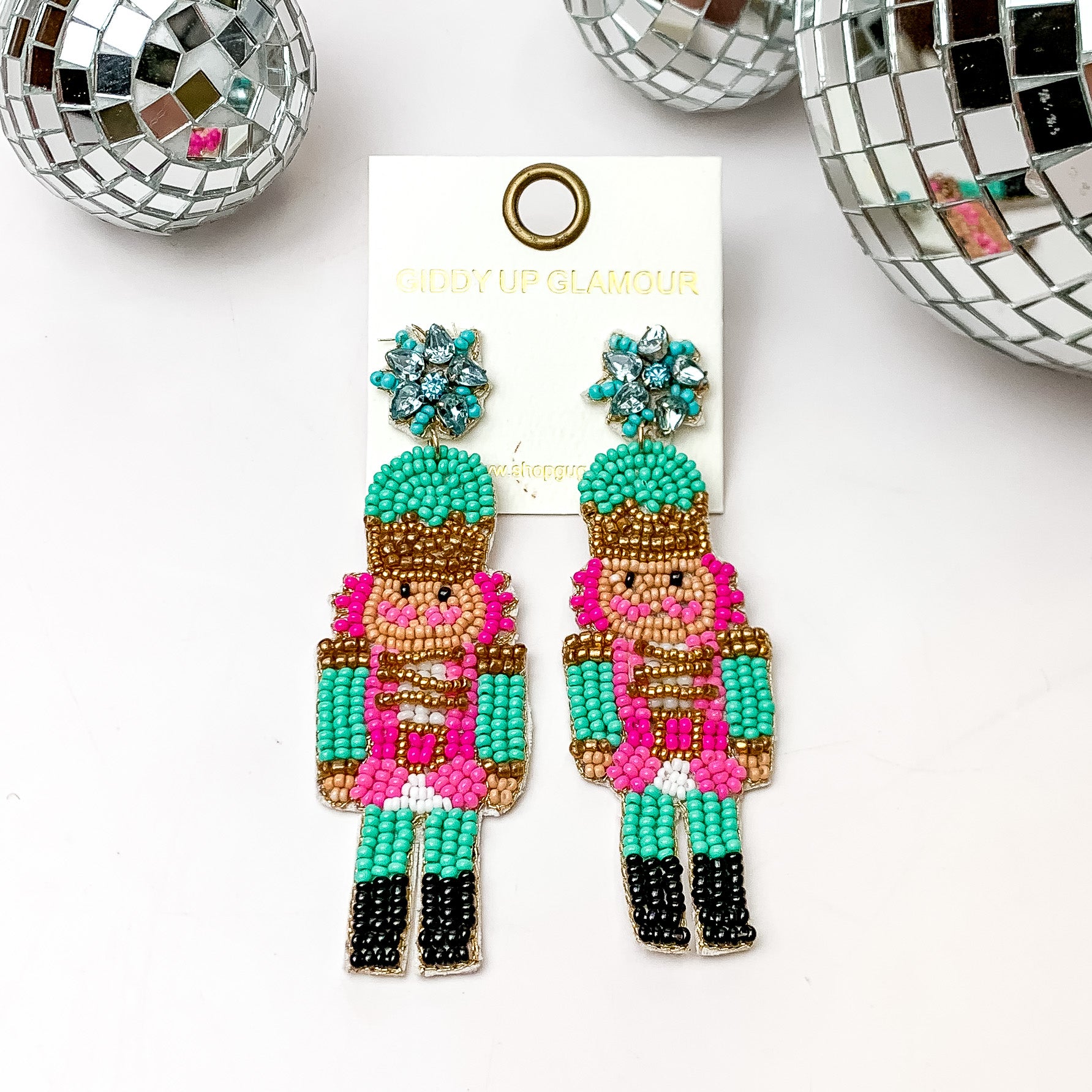 Beaded nutcracker earrings in turquoise and pink. These earrings are pictured on a white background with disco balls at the top. 