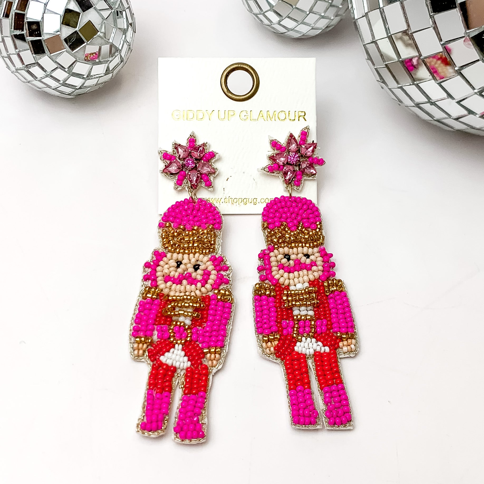 Beaded nutcracker earrings in red and pink. These earrings are pictured on a white background with disco balls at the top. 