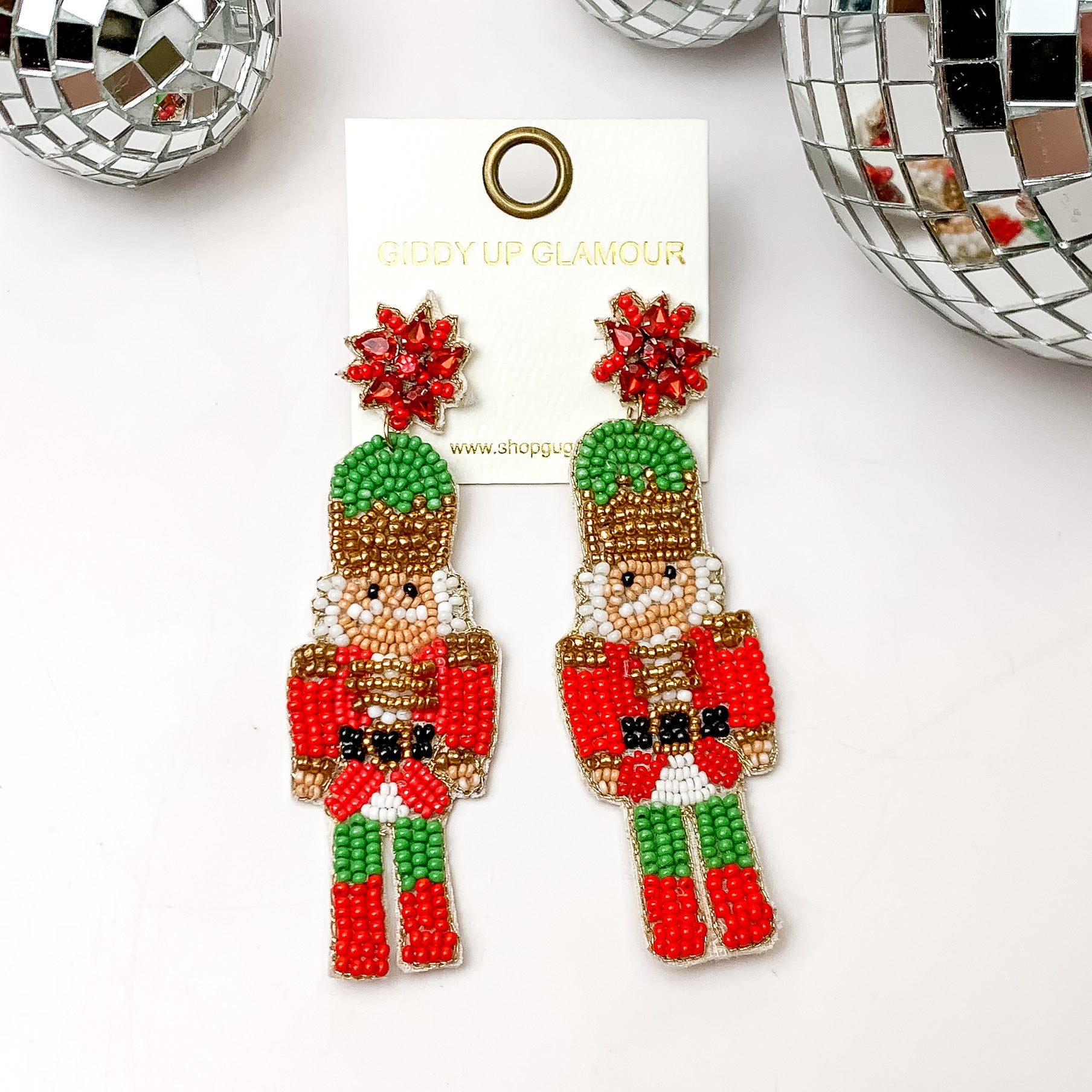 Beaded nutcracker earrings in red and green. These earrings are pictured on a white background with disco balls at the top. 