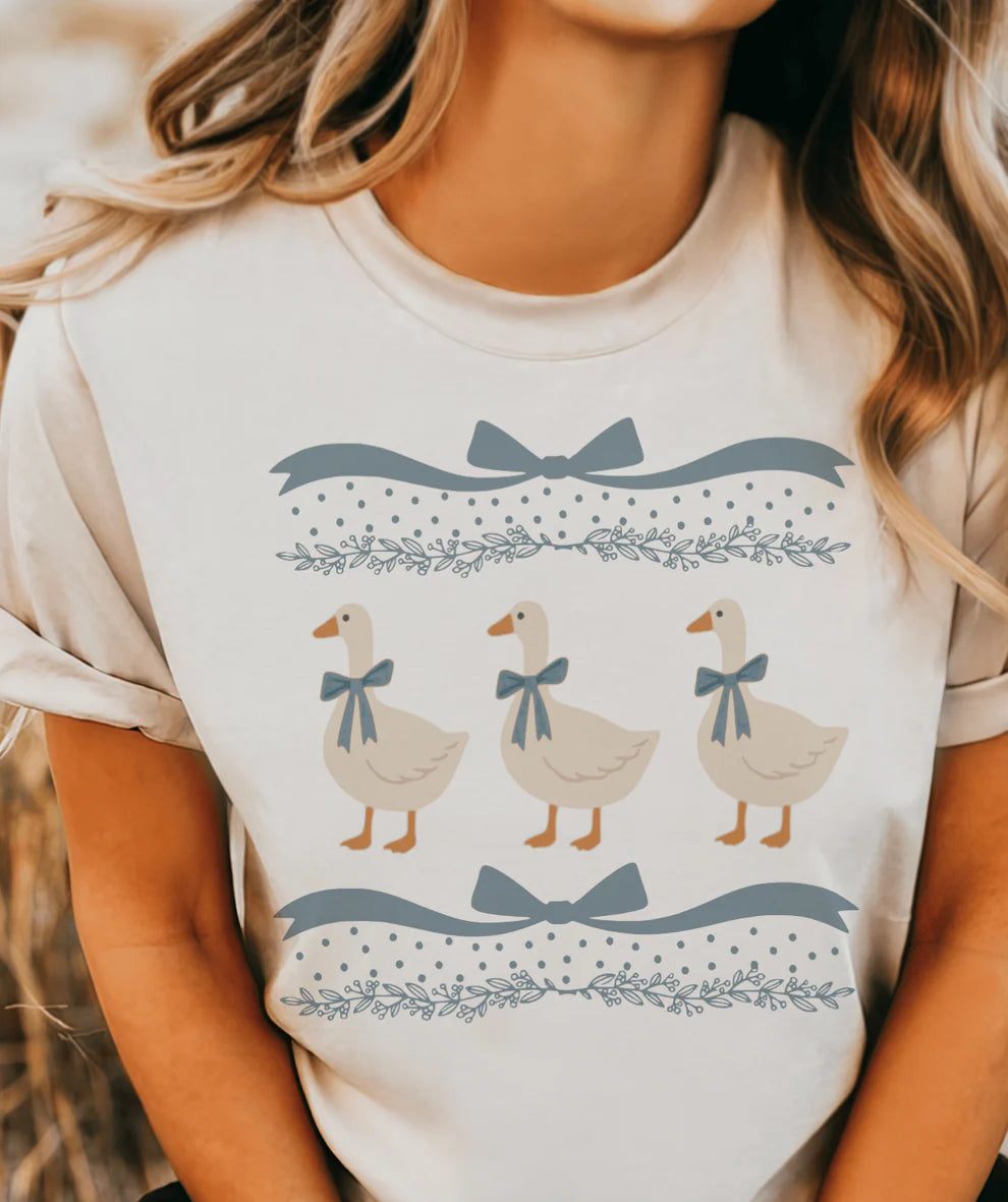 Blue Ribbon Goose graphic tee featuring three geese with blue ribbon bows on a cream cottagecore shirt.