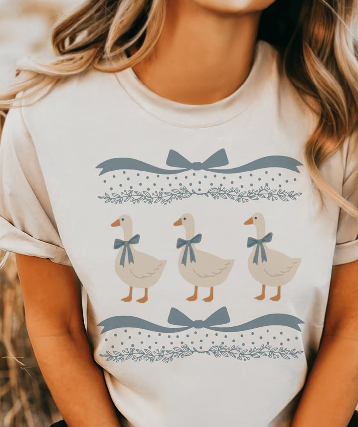 Blue Ribbon Goose graphic tee featuring three geese with blue ribbon bows on a cream cottagecore shirt.