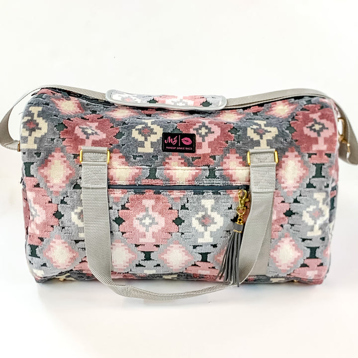 Pictured on a white background is a duffel bag with grey straps in a blush aztec print. This bag includes a zipper tassel, two short grey straps, and a grey tan strap.