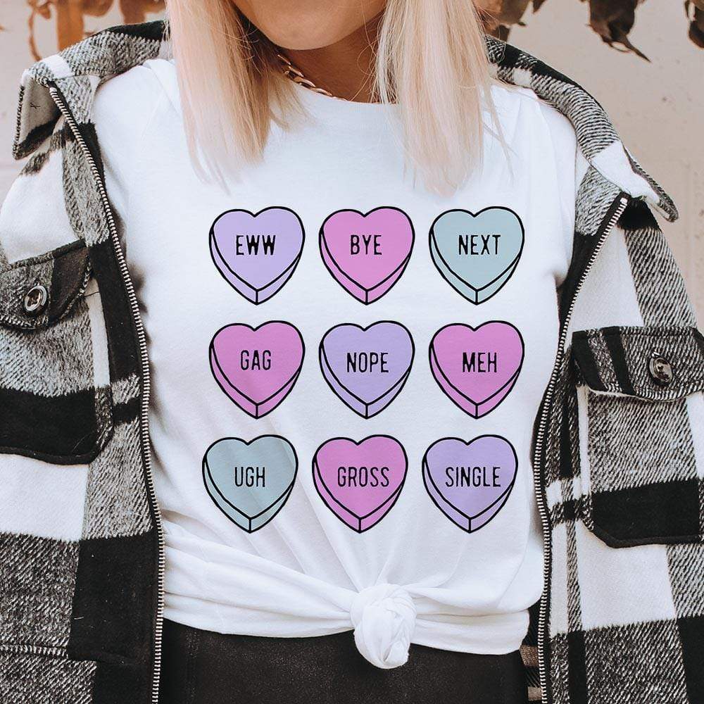 Model is wearing a white graphic tee that is knotted in the front. The tee shirt has candy hearts with gag words written across.