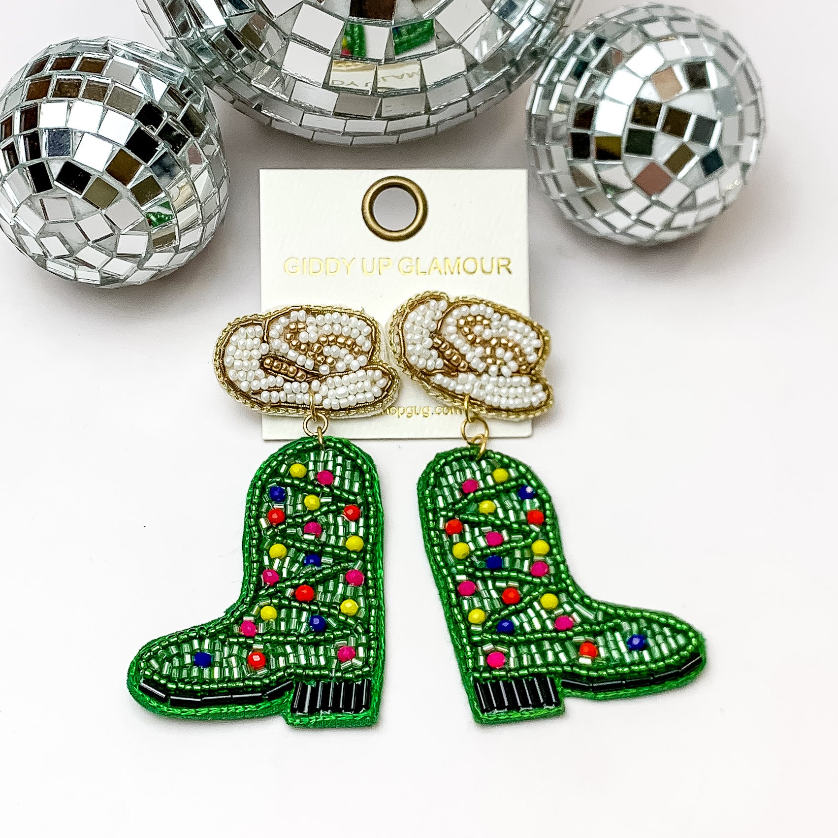 White and gold hat post earrings with green christmas tree boot shaped earrings. These earrings are pictured on a white background with disco balls at the top. 