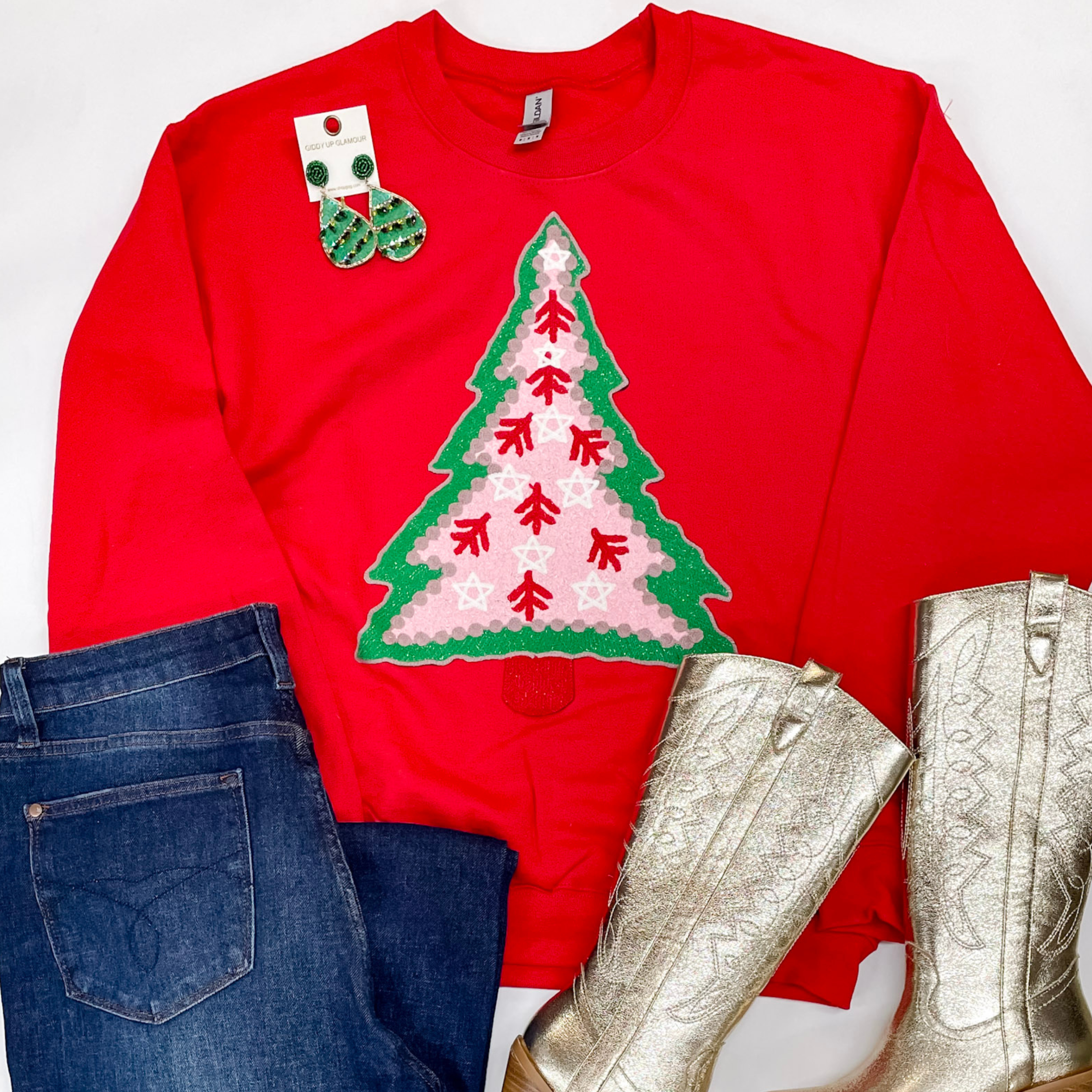 Photo features a red sweatshirt with a hand stitched christmas tree. This is paired with Judy Blue jeans, gold boots, and green earrings all on a white background.