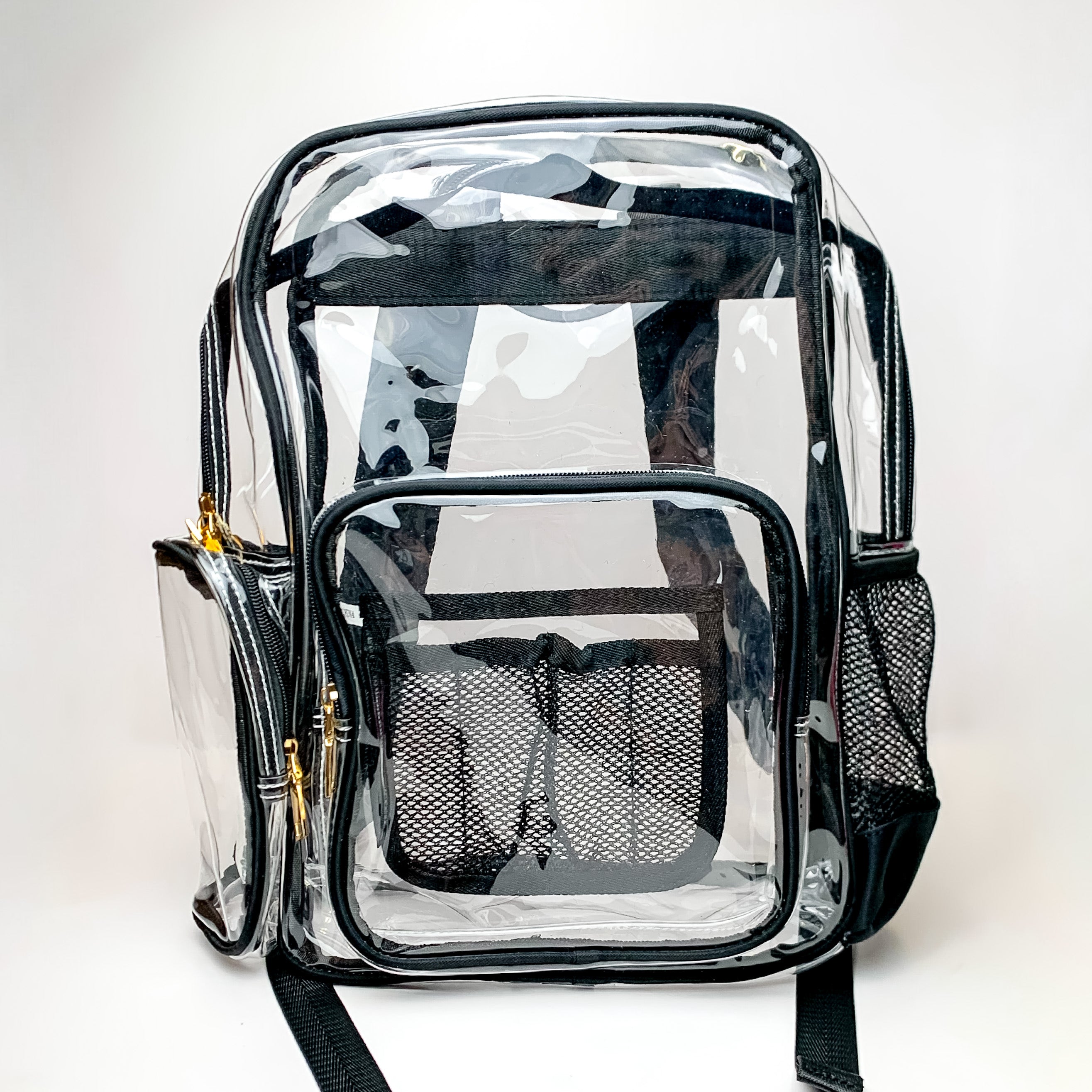 Pictured on a white background is a clear backpack with a black outline, black mesh pockets, and gold hardware. 