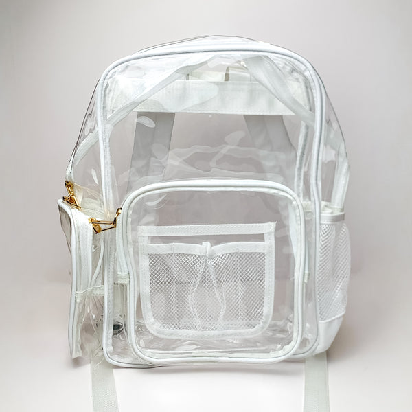 Pictured on a white background is a clear backpack with a white outline, white mesh pockets, and gold hardware. 