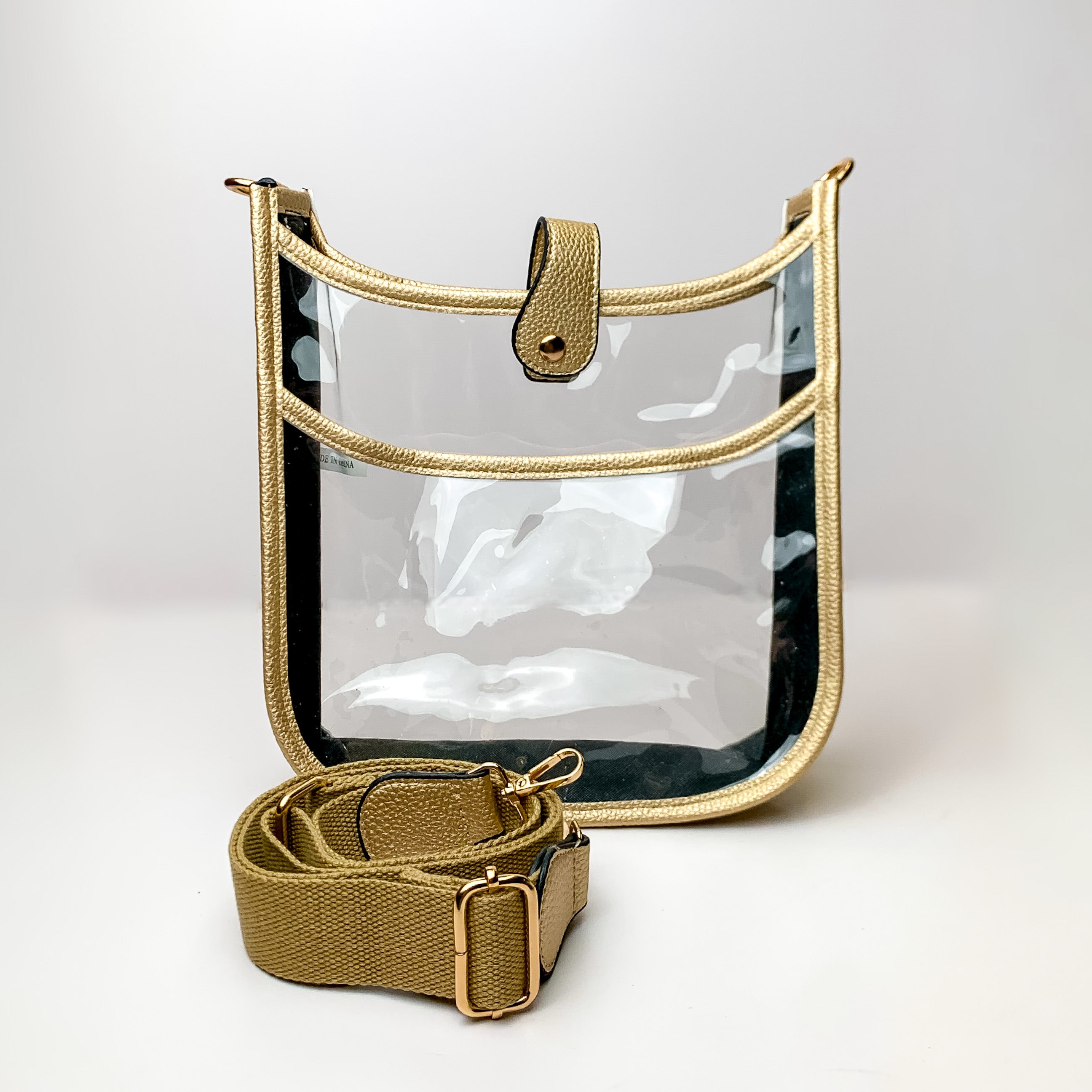 Clear crossbody purse in gold with a gold purse strap pictured in front of the purse. This purse is pictured on a white background. 