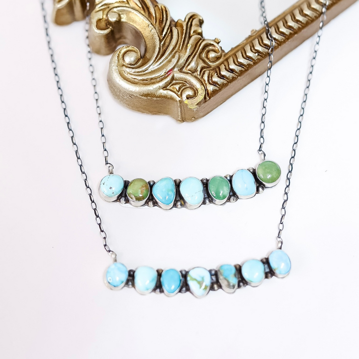Sterling silver bar necklace with multi-tone turquoise stones handcrafted by Navajo artist Scott Skeets, displayed on ornate gold mirror.