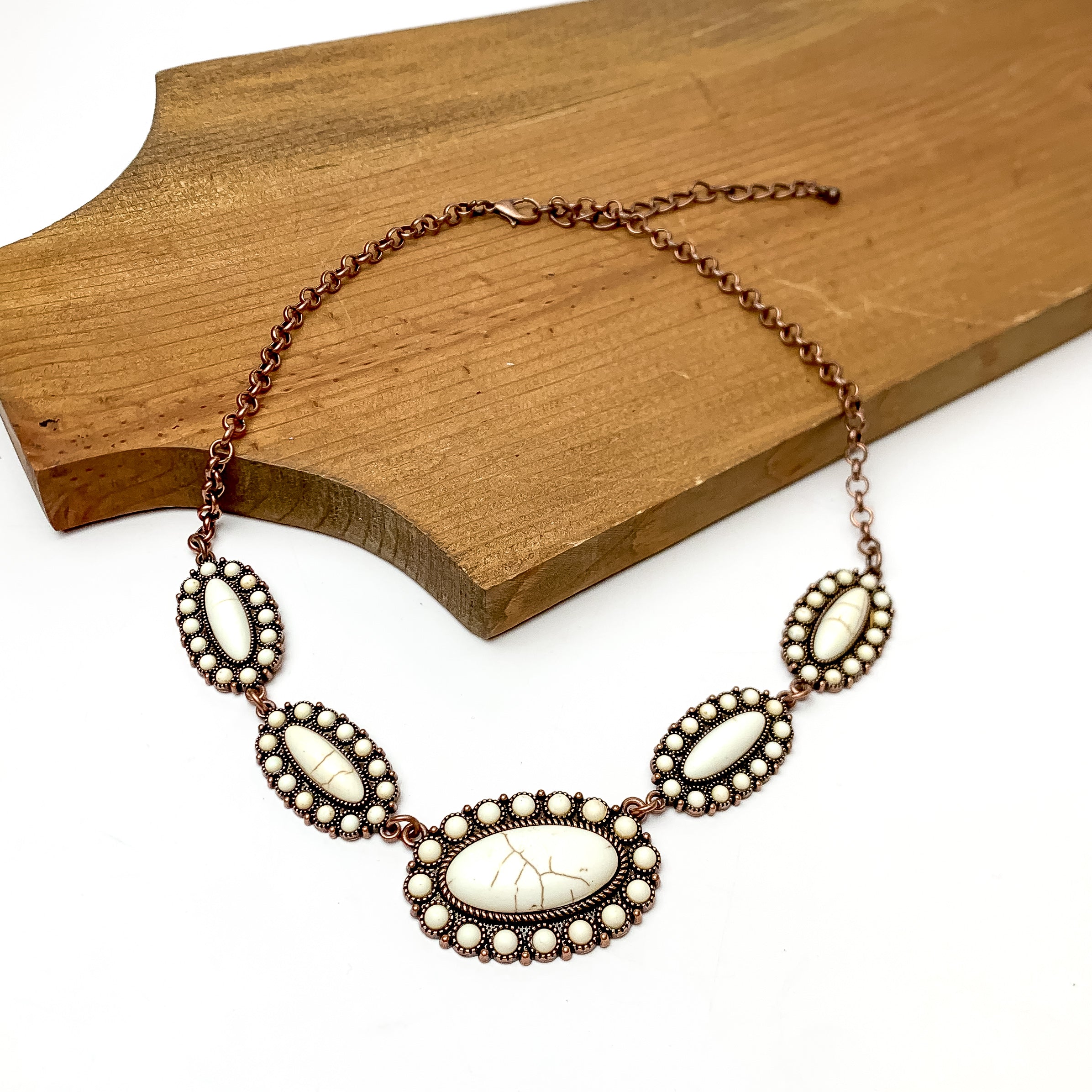 Western Copper Tone Necklace in Ivory. This necklace is pictured paying on a wood piece with a white background.
