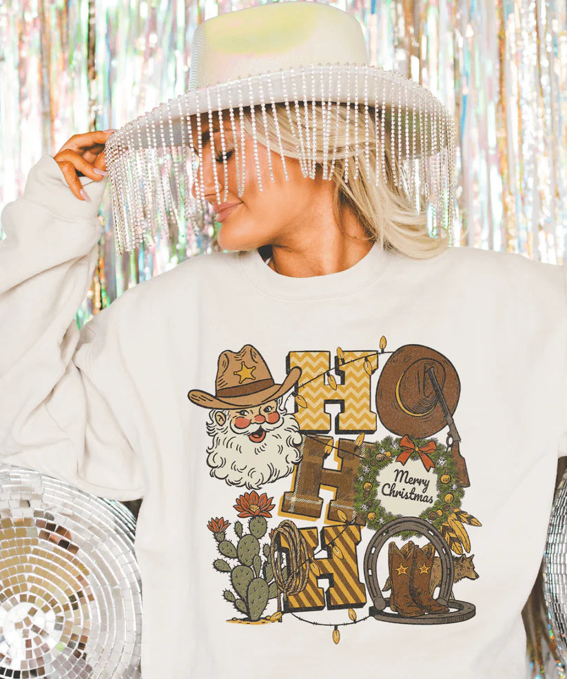 Cowboy Santa “Ho Ho Ho” graphic tee showing western Santa with hat, boots, wreath, and cacti on a cream tee.