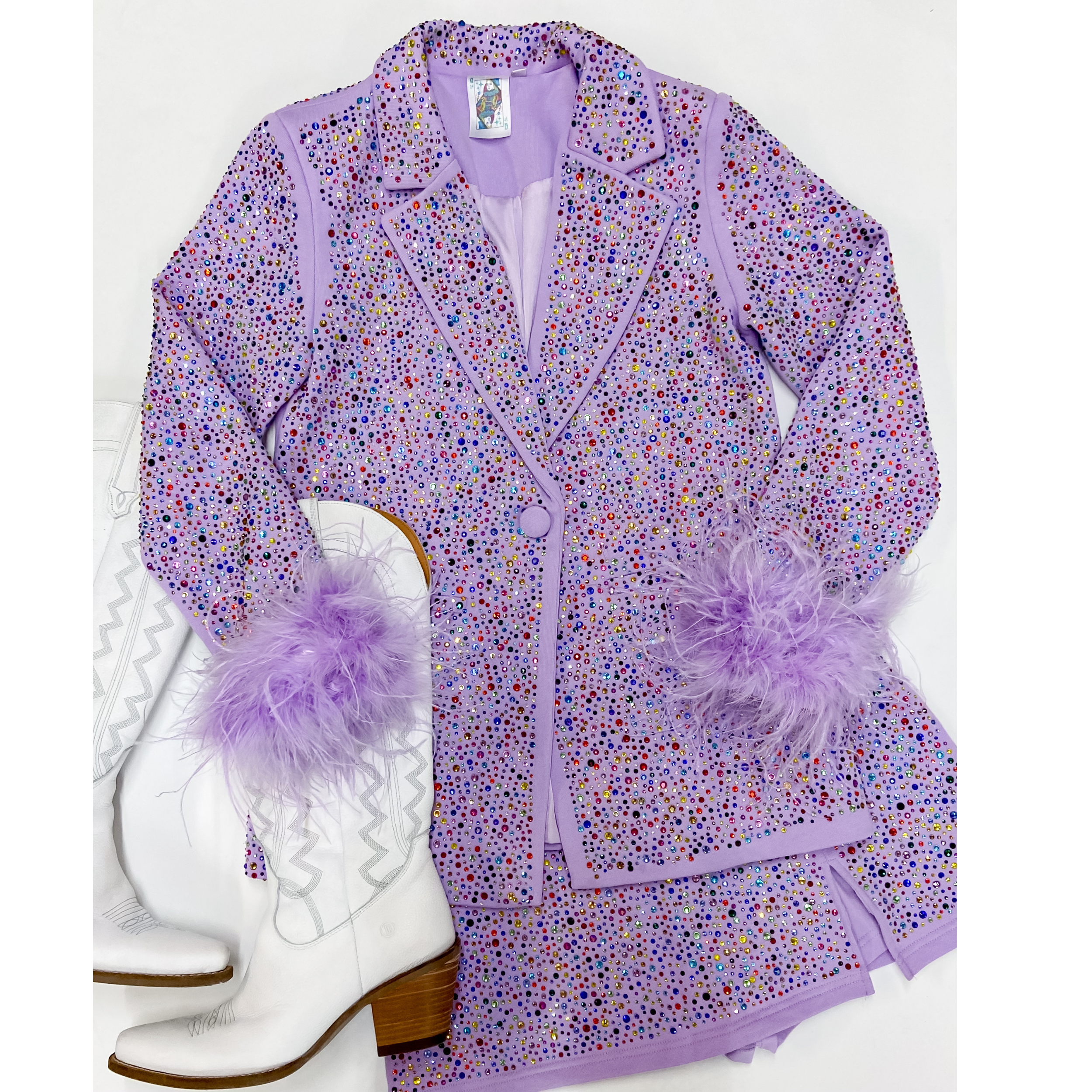 Photo features crystal studded lavender blazer with feathers cuffs around the wrists. This balzer is pictures on an all white background with white boots.  