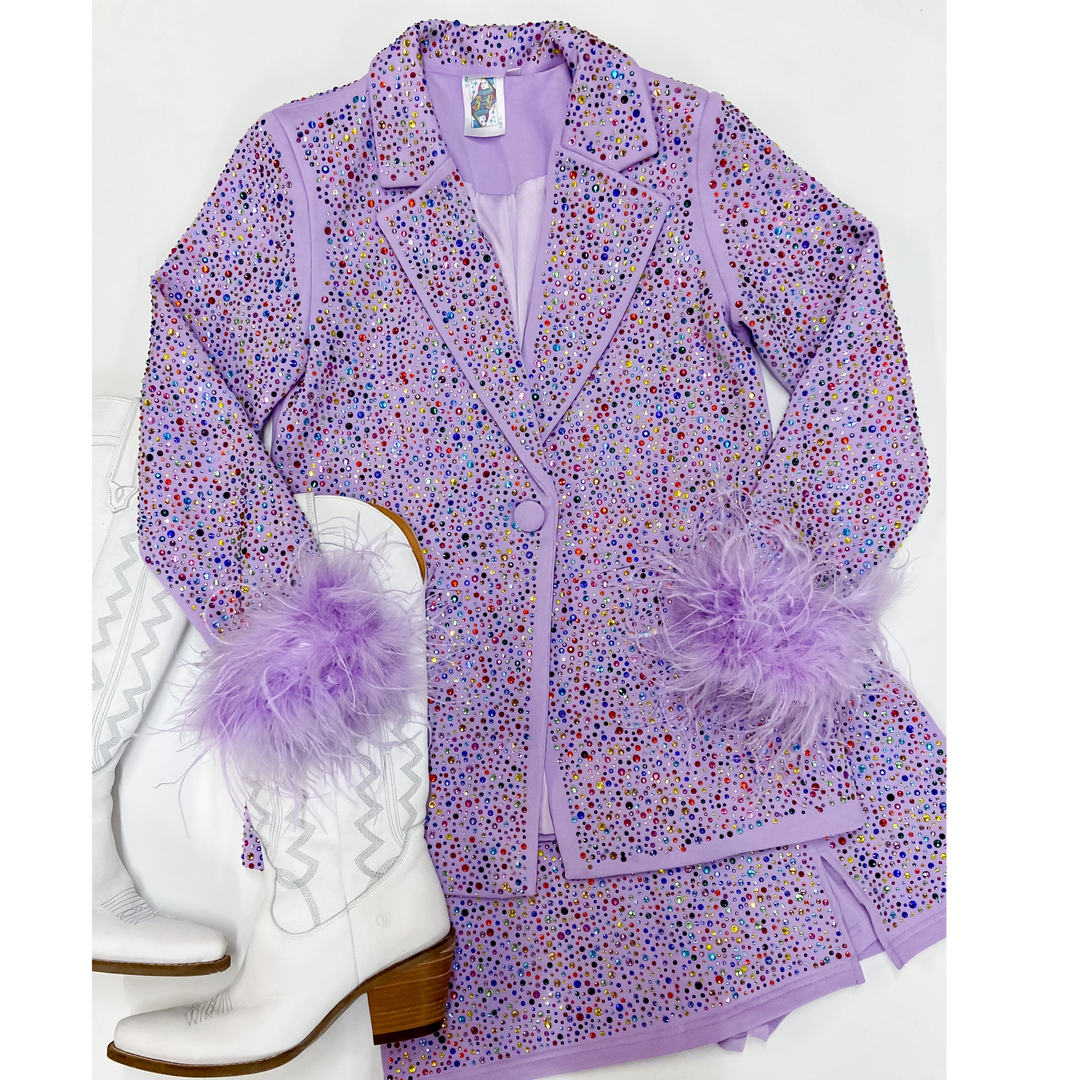 Photo features crystal studded lavender blazer with feathers cuffs around the wrists. This balzer is pictures on an all white background with white boots.  