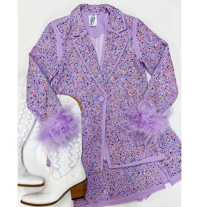 Photo features crystal studded lavender blazer with feathers cuffs around the wrists. This balzer is pictures on an all white background with white boots.  
