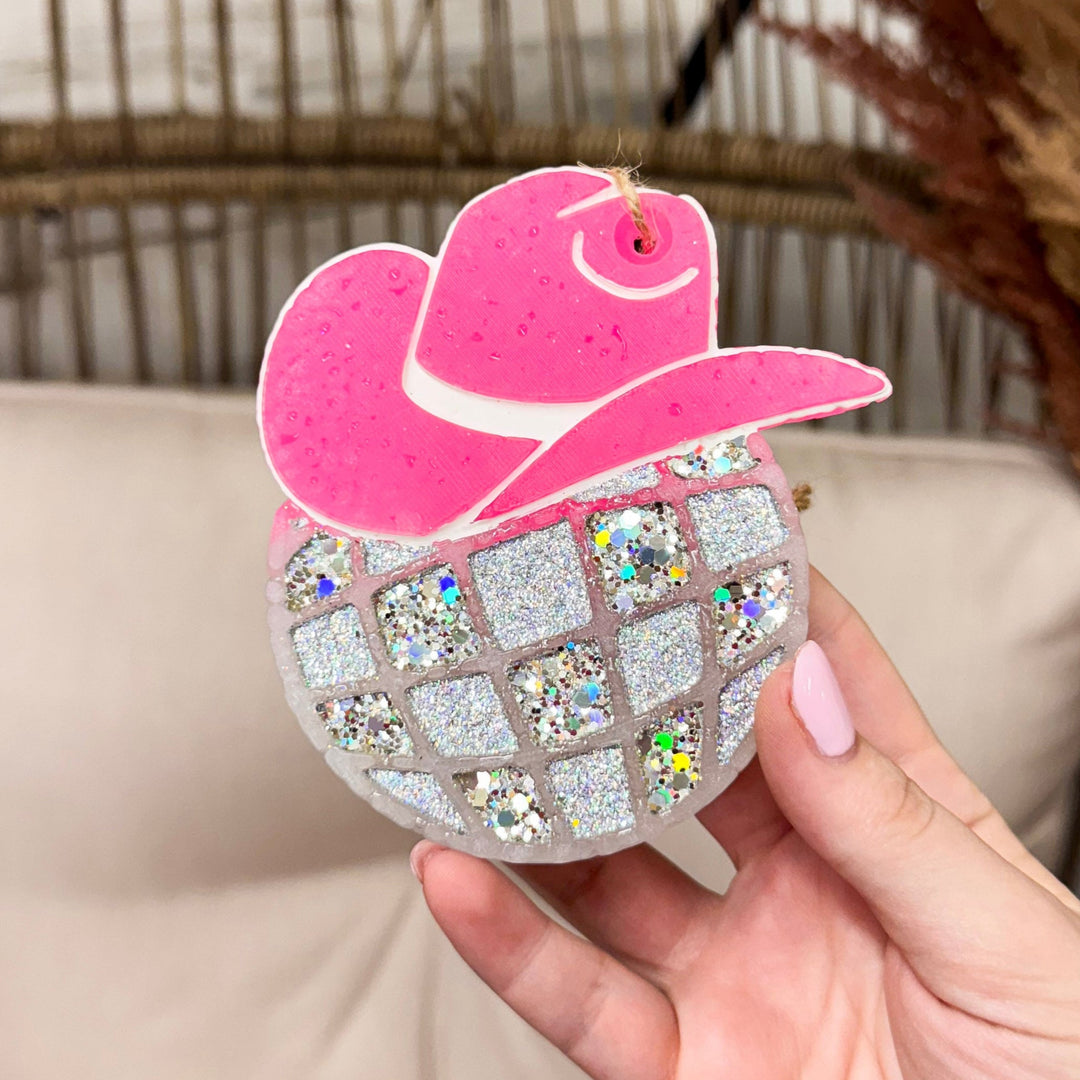 A hand holding a cowgirl disco hat car freshie with pink hat and silver glittery disco ball scent.