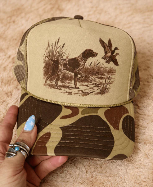 Olive and camouflage trucker hat featuring a vintage hunting dog and duck scene with an adjustable mesh back.