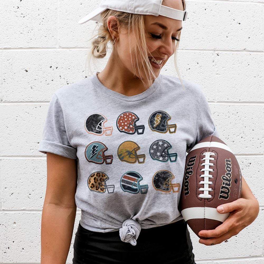 Model is wearing a gray short sleeve crewneck tee featuring a graphic of 9 football helmets, each with their unique pattern.