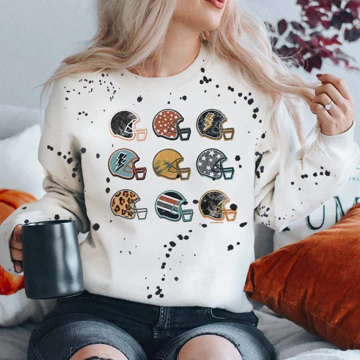 Model is wearing a white sweatshirt featuring a black splatter design and a graphic of 9 football helmets, each with their own unique design.