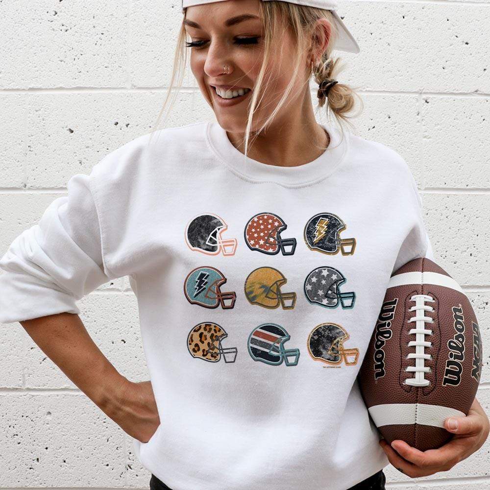 Model is wearing a white sweatshirt featuring a graphic of 9 football helmets, each with their unique pattern.