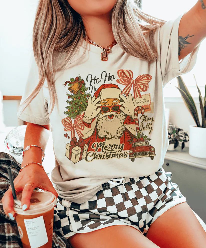 Cream tee with retro Santa collage design featuring gifts, bows, and a Stay Jolly message – vintage Christmas graphic from Giddy Up Glamour.